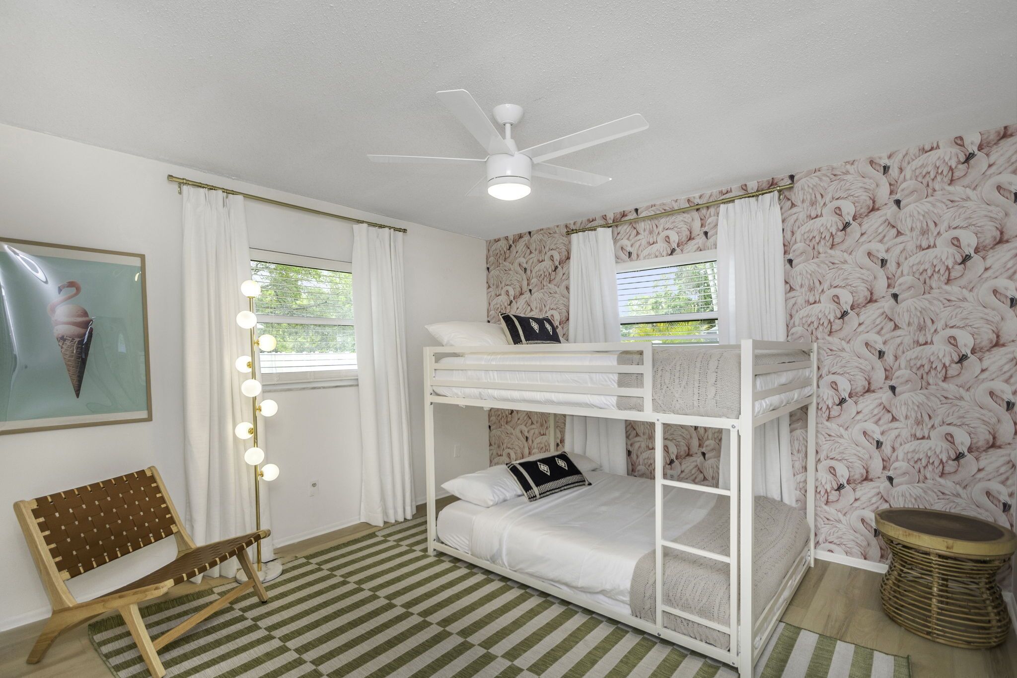 Een slaapkamer met stapelbed, plafondventilator, een bank en een muur met flamingo’s.