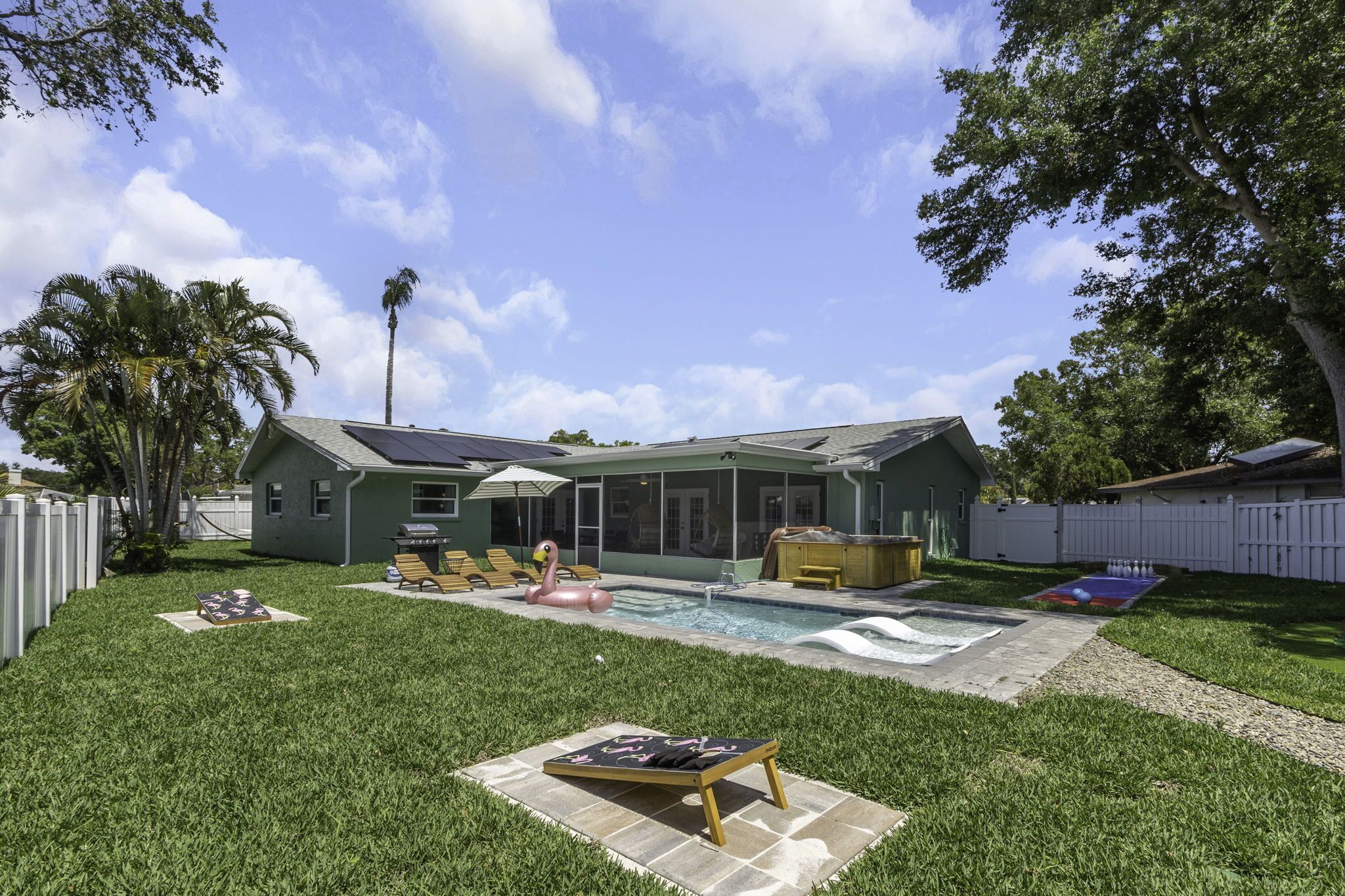 Un jardin avec une piscine, un jacuzzi et un espace patio aménagé avec des chaises longues et un flotteur en forme de flamant rose.