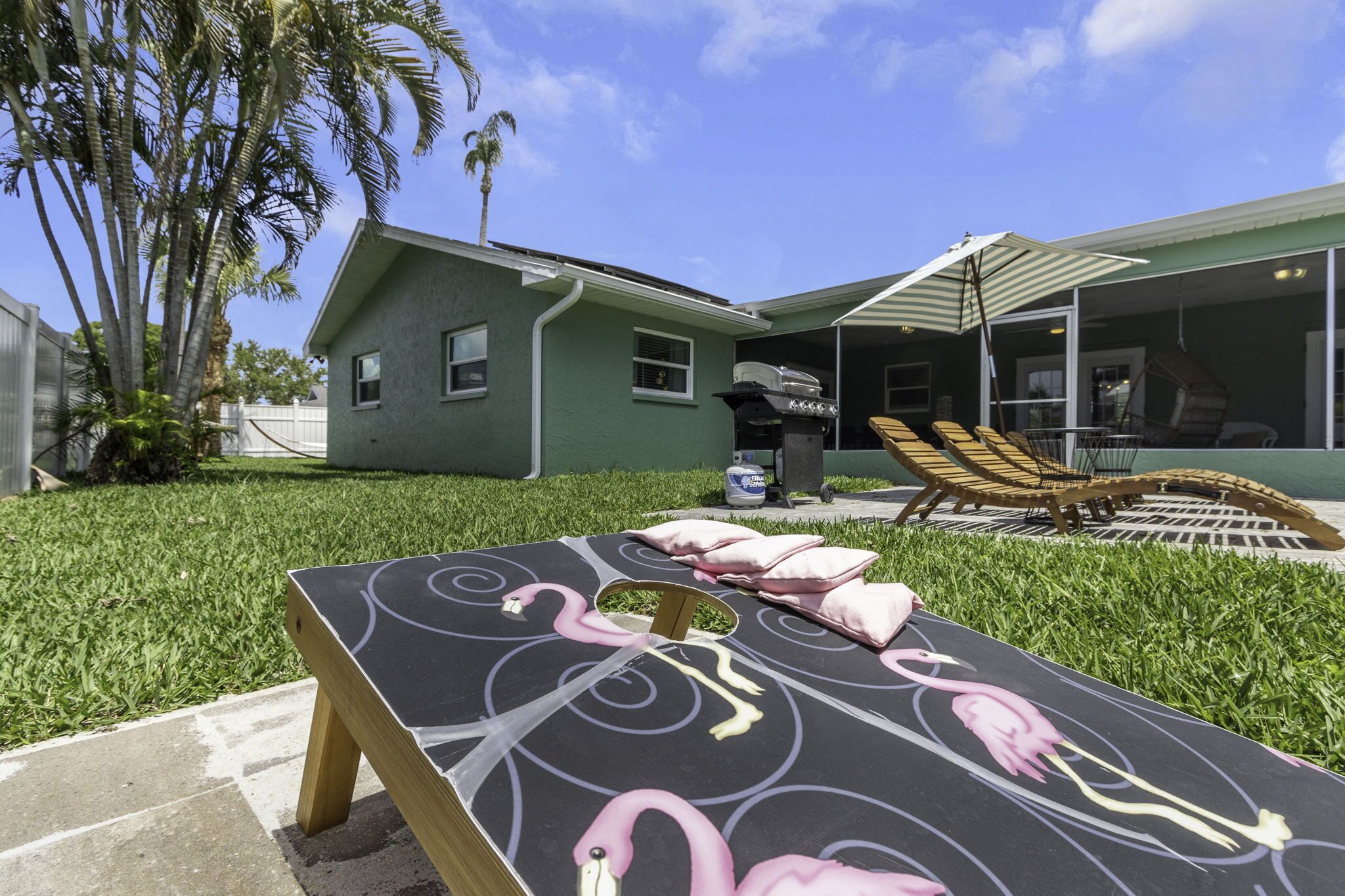 A pool table with flamingo designs, a covered outdoor seating area with lounge chairs, and a house with a green exterior.