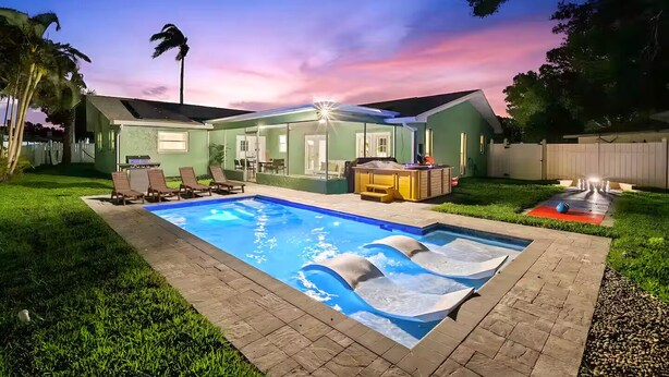 Un patio trasero con piscina, sillas de descanso y un jacuzzi.