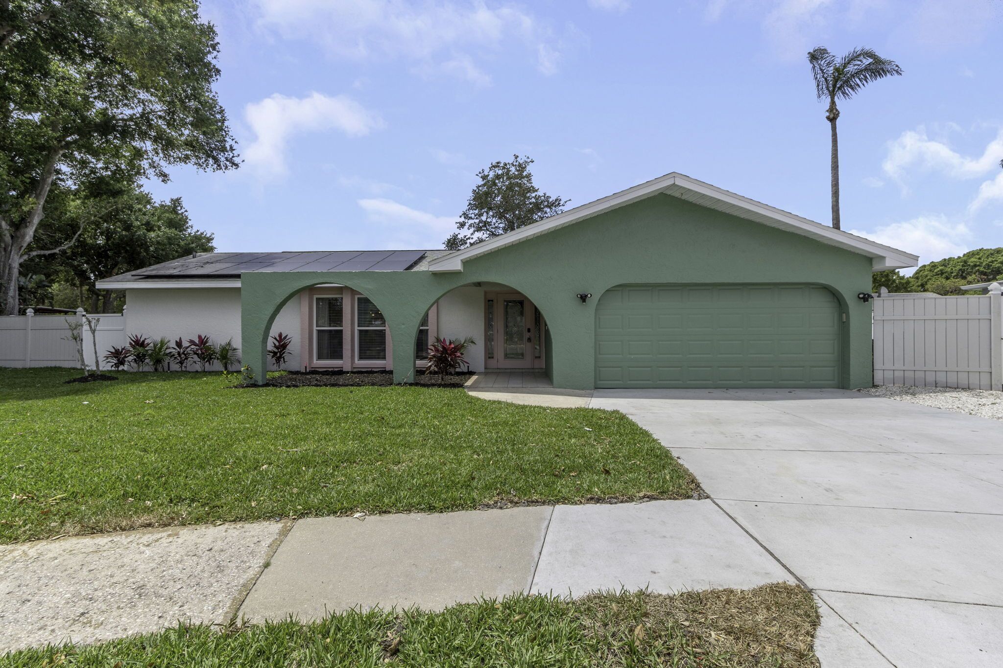 A single-story house with a green garage door, a covered porch, and a solar panel on the roof.