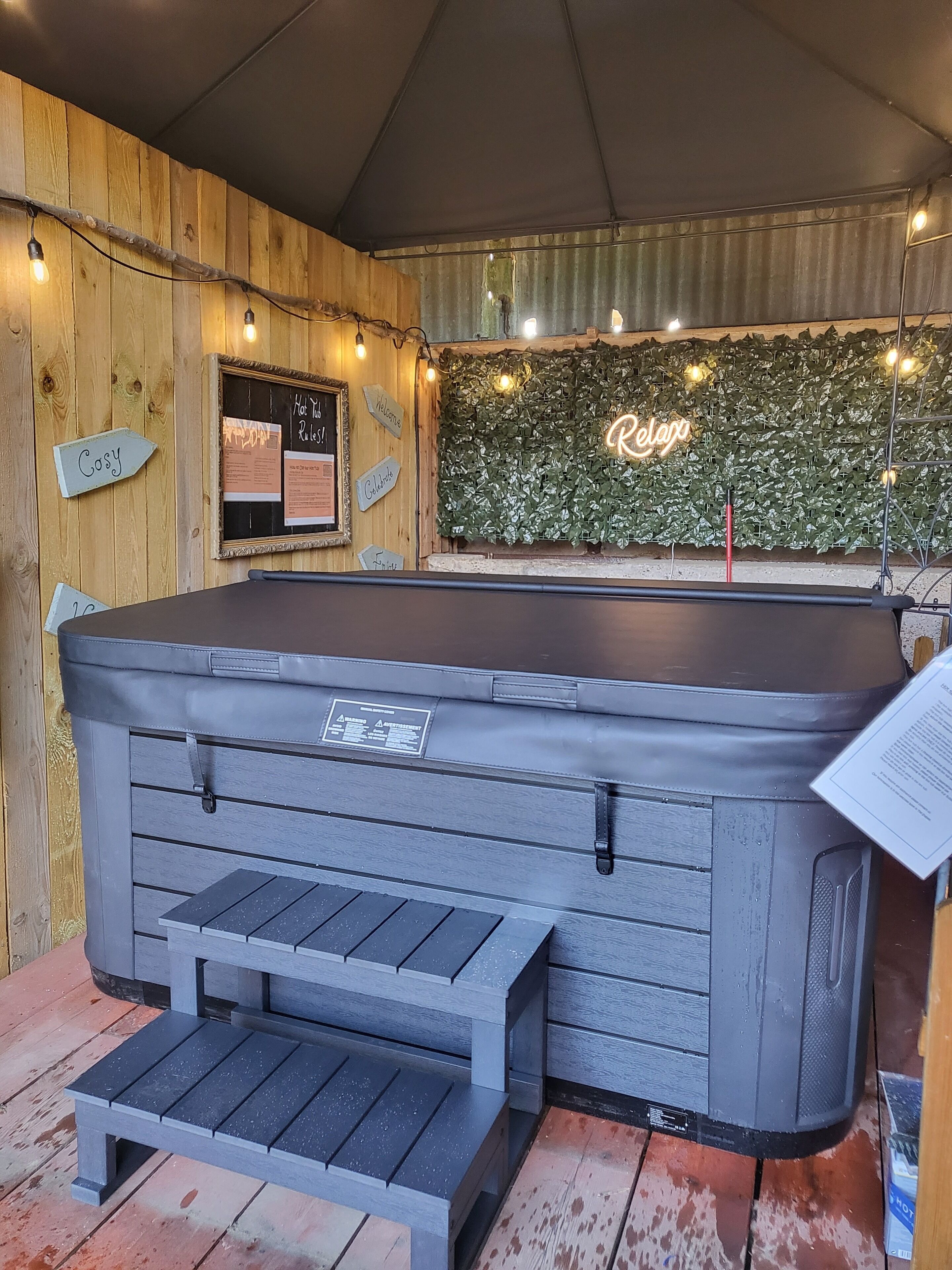 Ein Whirlpool mit Holzwand im Hintergrund, ein Neon-Leuchtschild und eine Bank.