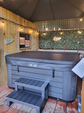 Ein Whirlpool mit Holzwand im Hintergrund, ein Neon-Leuchtschild und eine Bank.