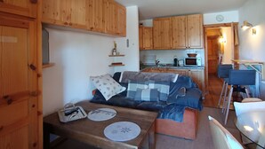 Een compact woongedeelte met een kitchenette, houten kastjes, een bank en een eethoek.