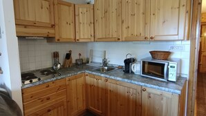 Een kleine keuken met houten kastjes, een magnetron, een waterkoker en een spoelbak.