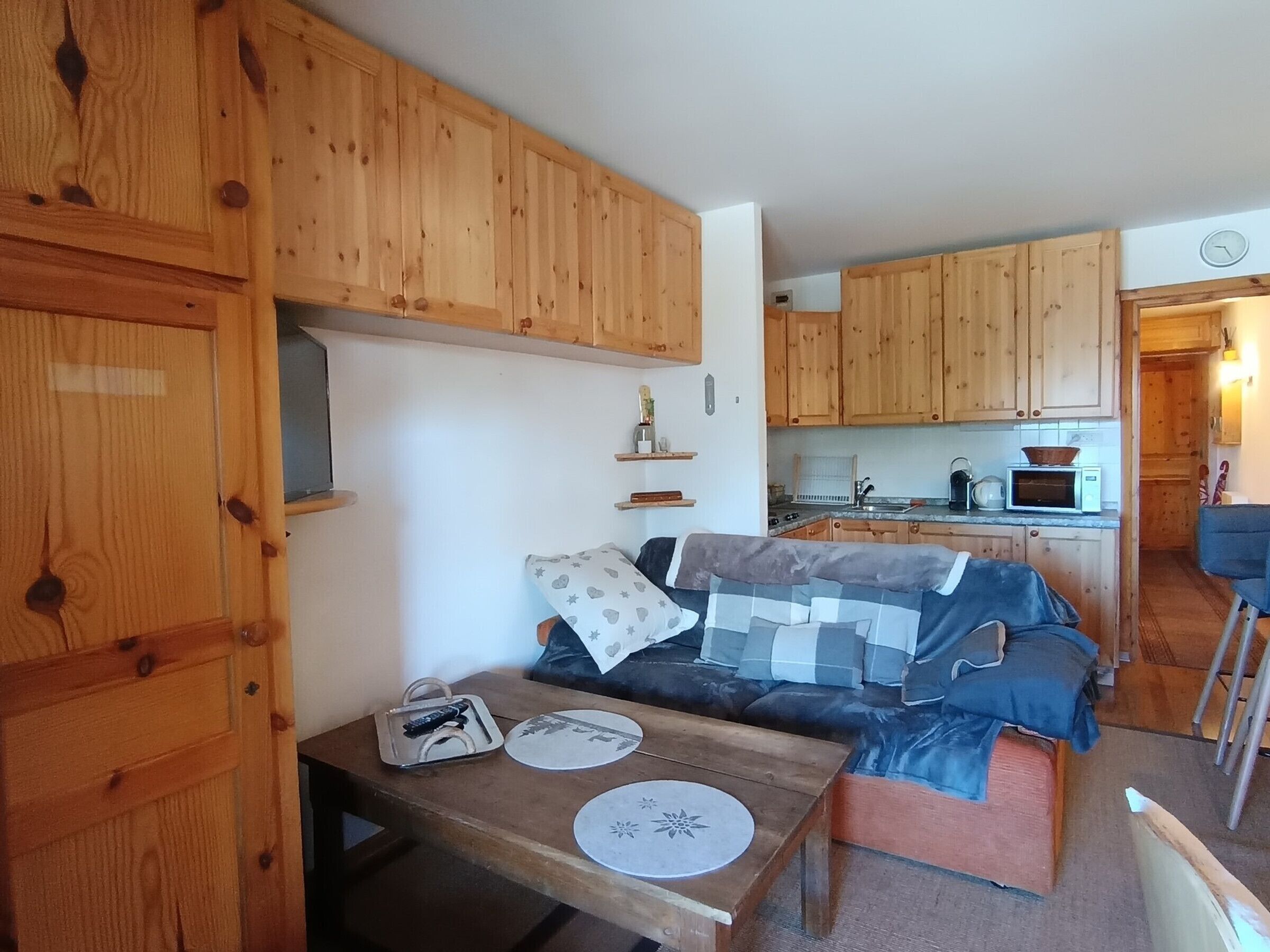 A cozy room with wooden cabinets, a kitchenette, a sofa with patterned cushions, and a small table with a tray and placemats.
