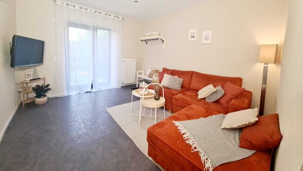 Una sala de estar moderna con sofá, televisión y comedor con mesa y sillas.