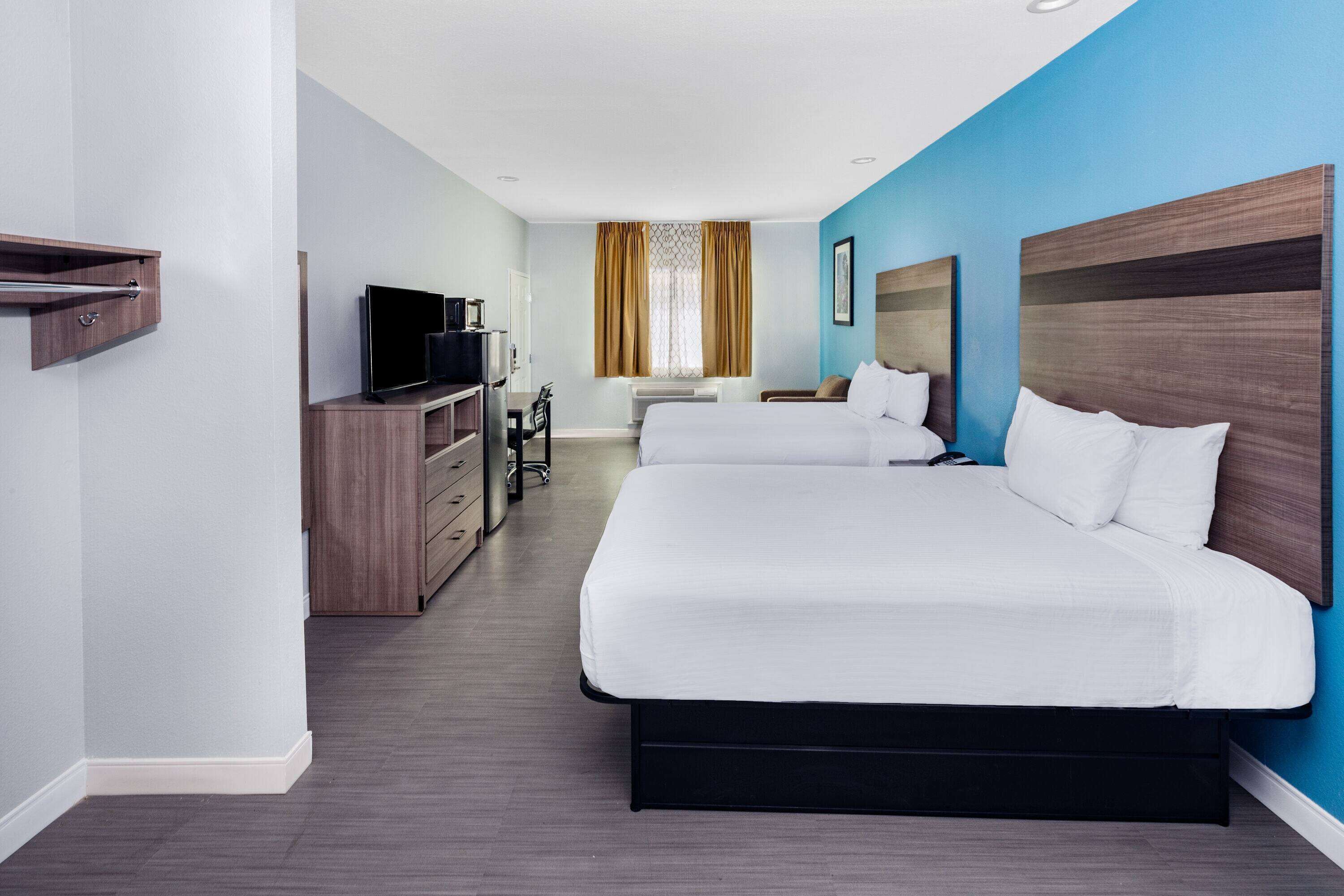 Habitación de hotel con dos camas, un escritorio con televisor, armario y ventana con cortinas.