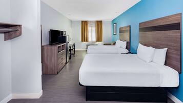 A hotel room with two beds, a desk with a TV, a wardrobe, and a window with curtains.