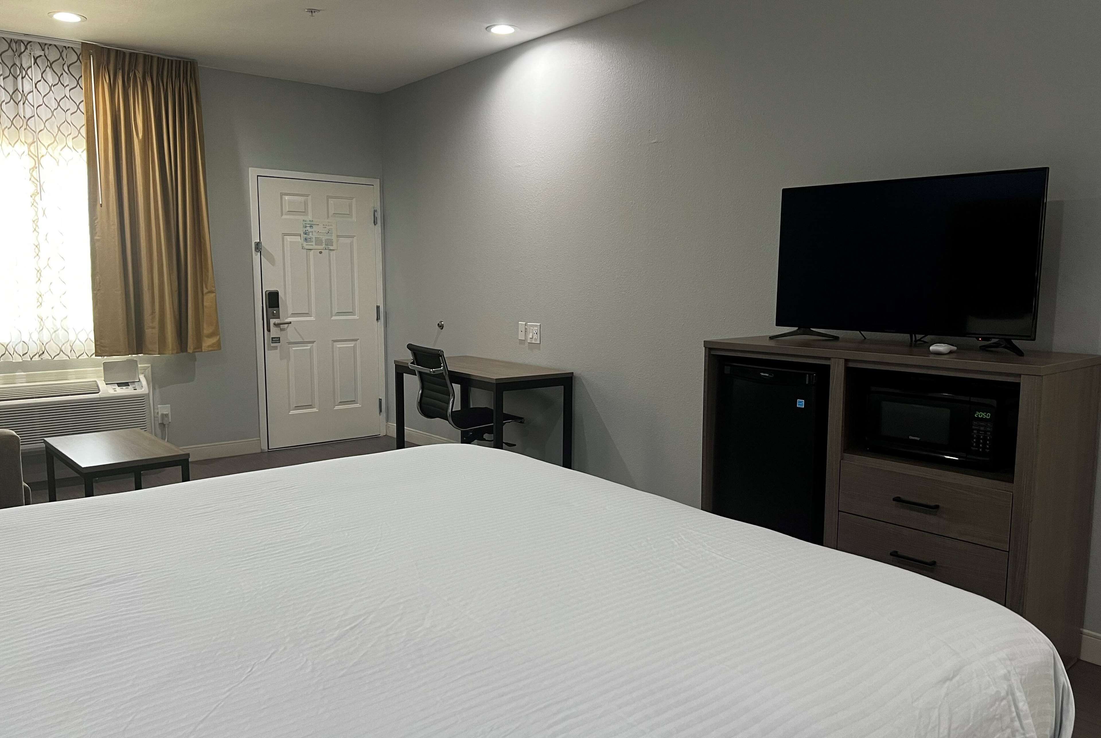 Ett hotellrum med en stor säng, ett skrivbord med en stol, en tv, en mikrovågsugn och en dörr.