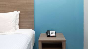 Una habitación de hotel con una cama, una mesita de noche y un teléfono, y una pared azul.