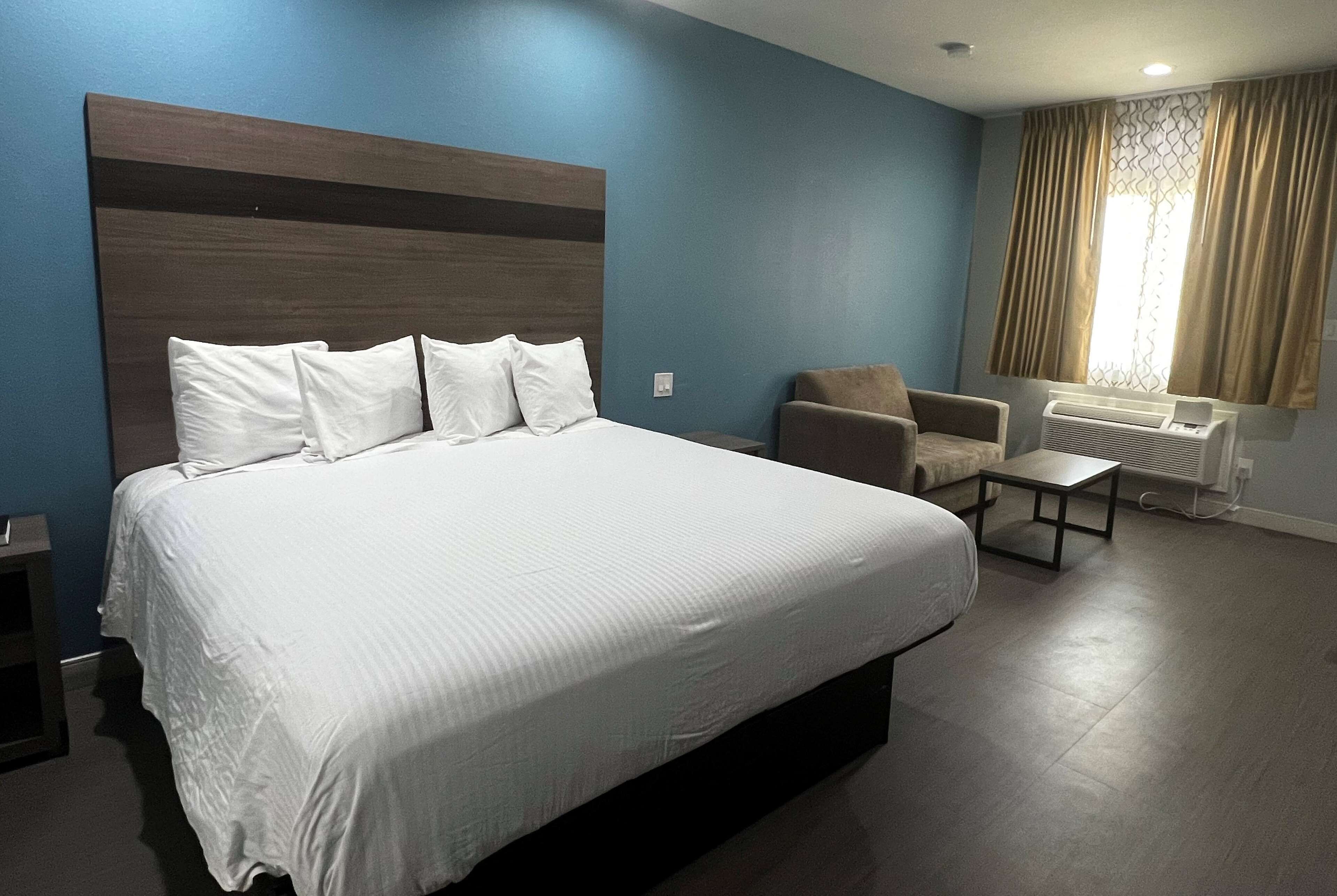 A hotel room with a large bed, a chair, a small table, and a window with curtains.
