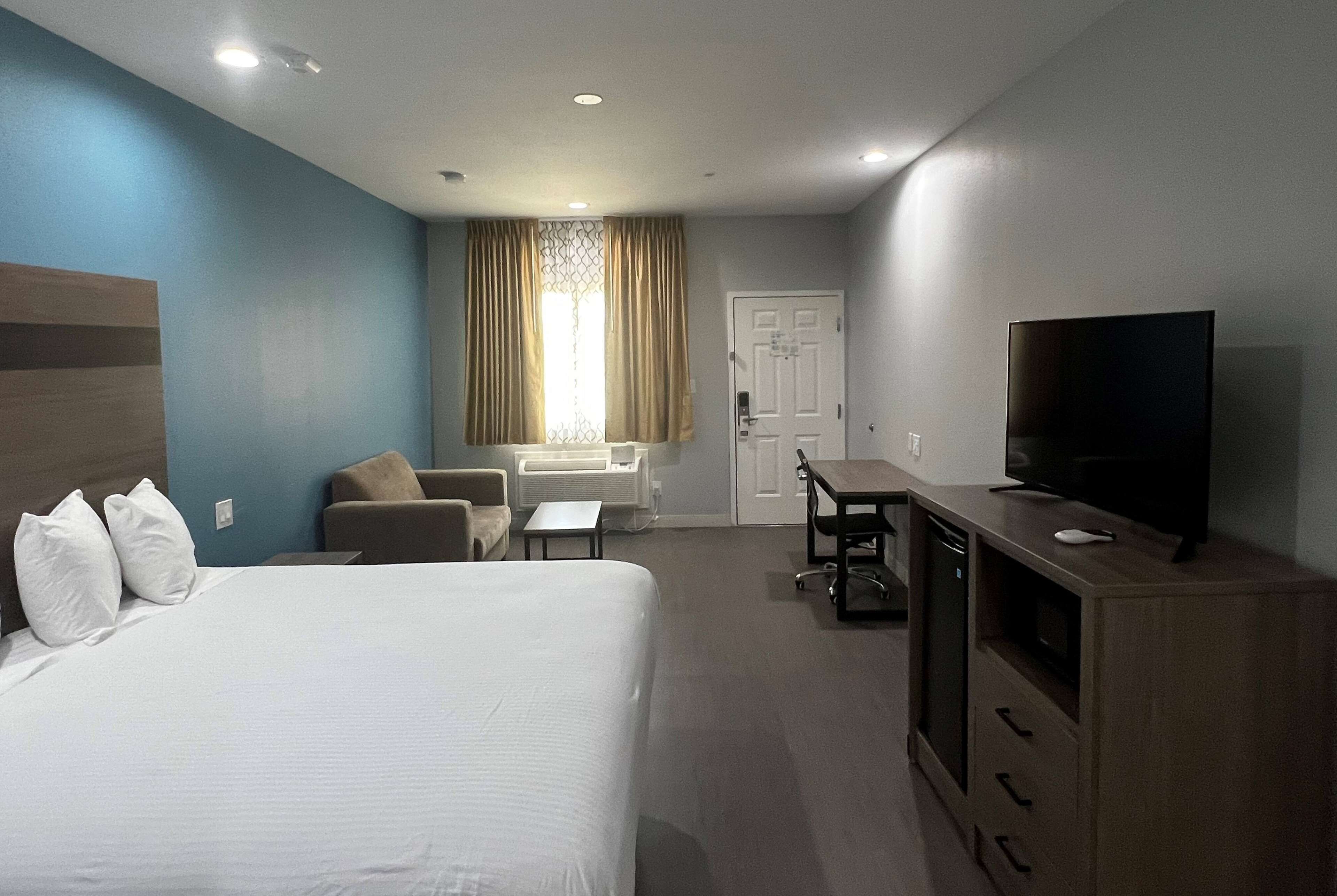 Une chambre d’hôtel comprenant un lit, un bureau, une télévision et un coin salon avec un fauteuil et un canapé.
