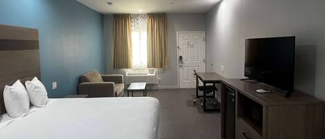 Une chambre d’hôtel comprenant un lit, un bureau, une télévision et un coin salon avec un fauteuil et un canapé.
