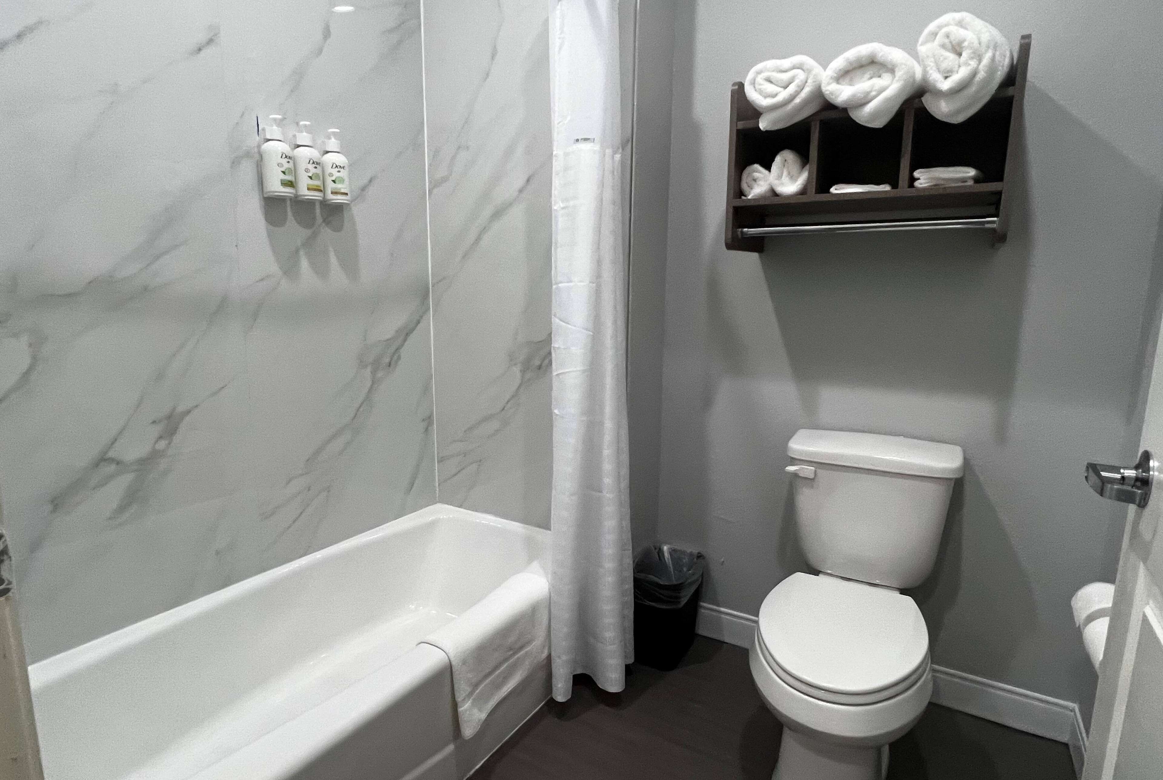 A bathroom with a bathtub, toilet, and a shelf with towels.