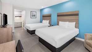 A hotel room with two beds, a desk, and a kitchenette.