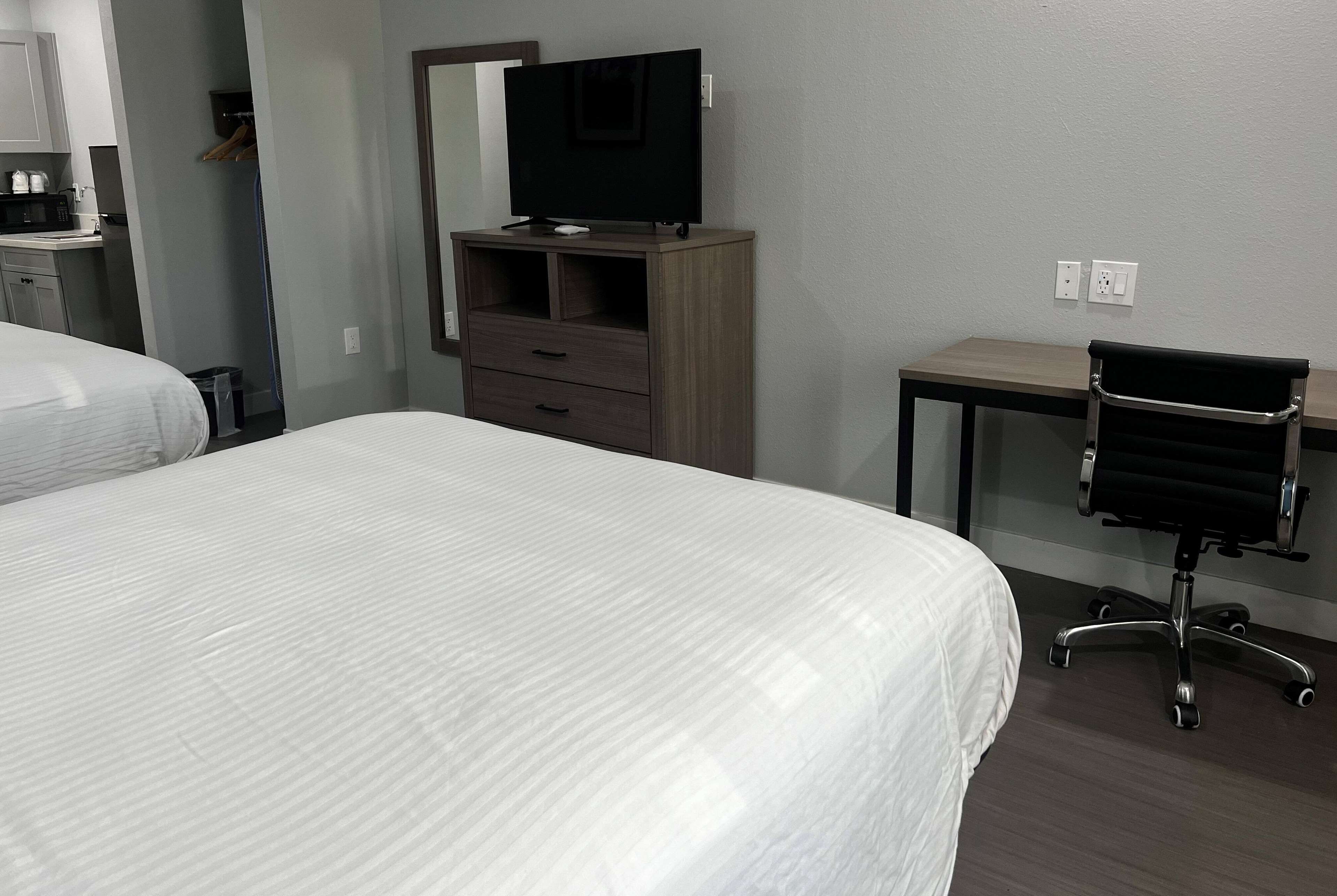 Una camera d'albergo con due letti, una TV su un mobile in legno, una scrivania con una sedia e uno specchio a parete.