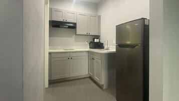 A compact kitchen with white cabinets, a stainless steel refrigerator, and a black cooking pot on the countertop.