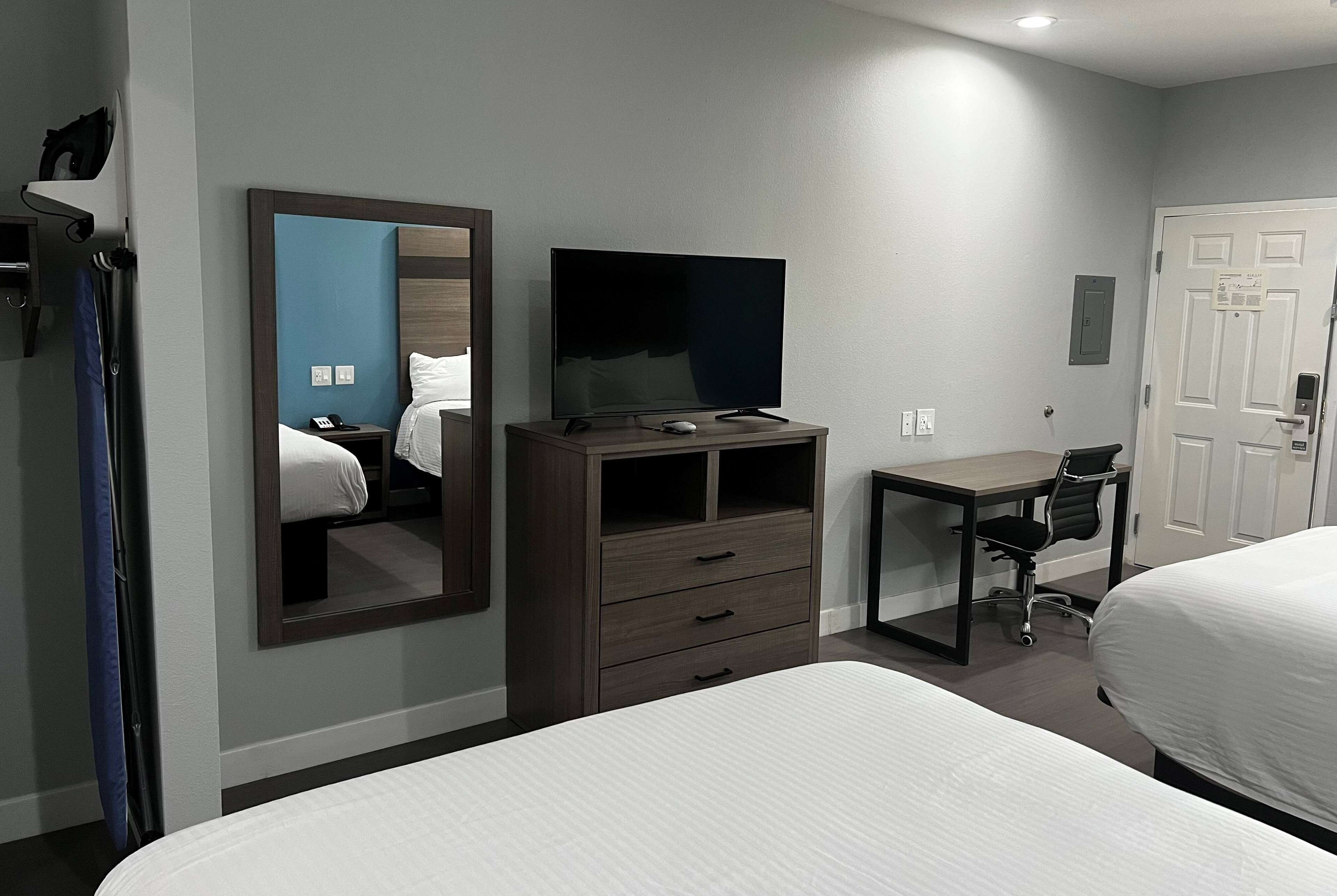 A hotel room with a bed, a desk with a chair, a television, and a mirror.