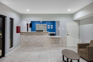 Una zona de recepción con pared azul, mostrador de ladrillo, puerta blanca y sillón color beige.