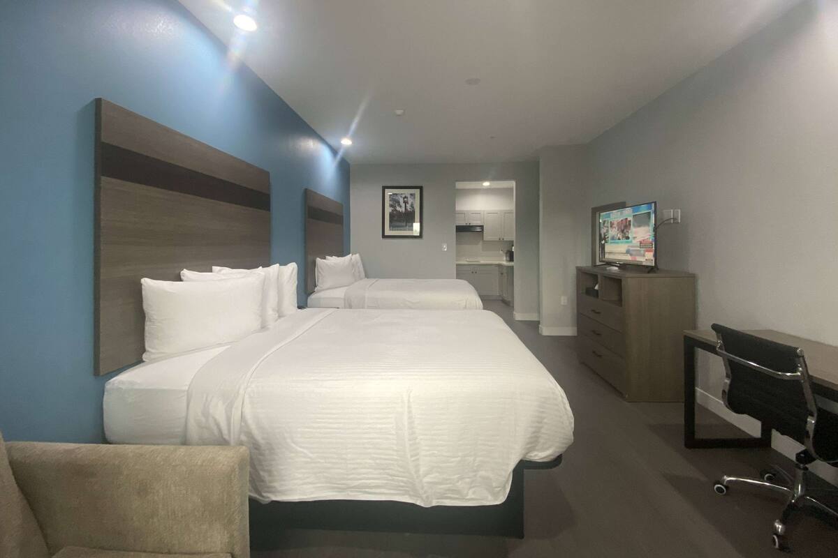 Ein Hotelzimmer mit einem großen Bett, einem Schreibtisch, einem Sessel und einer Küchenzeile im Hintergrund.
