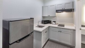 A compact kitchen with a stainless steel refrigerator, a microwave, a coffee maker, and a sink.