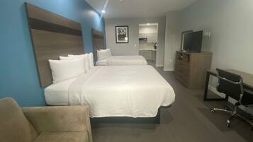 Habitación de hotel con una cama grande, un sofá, un televisor y una kitchenette al fondo.