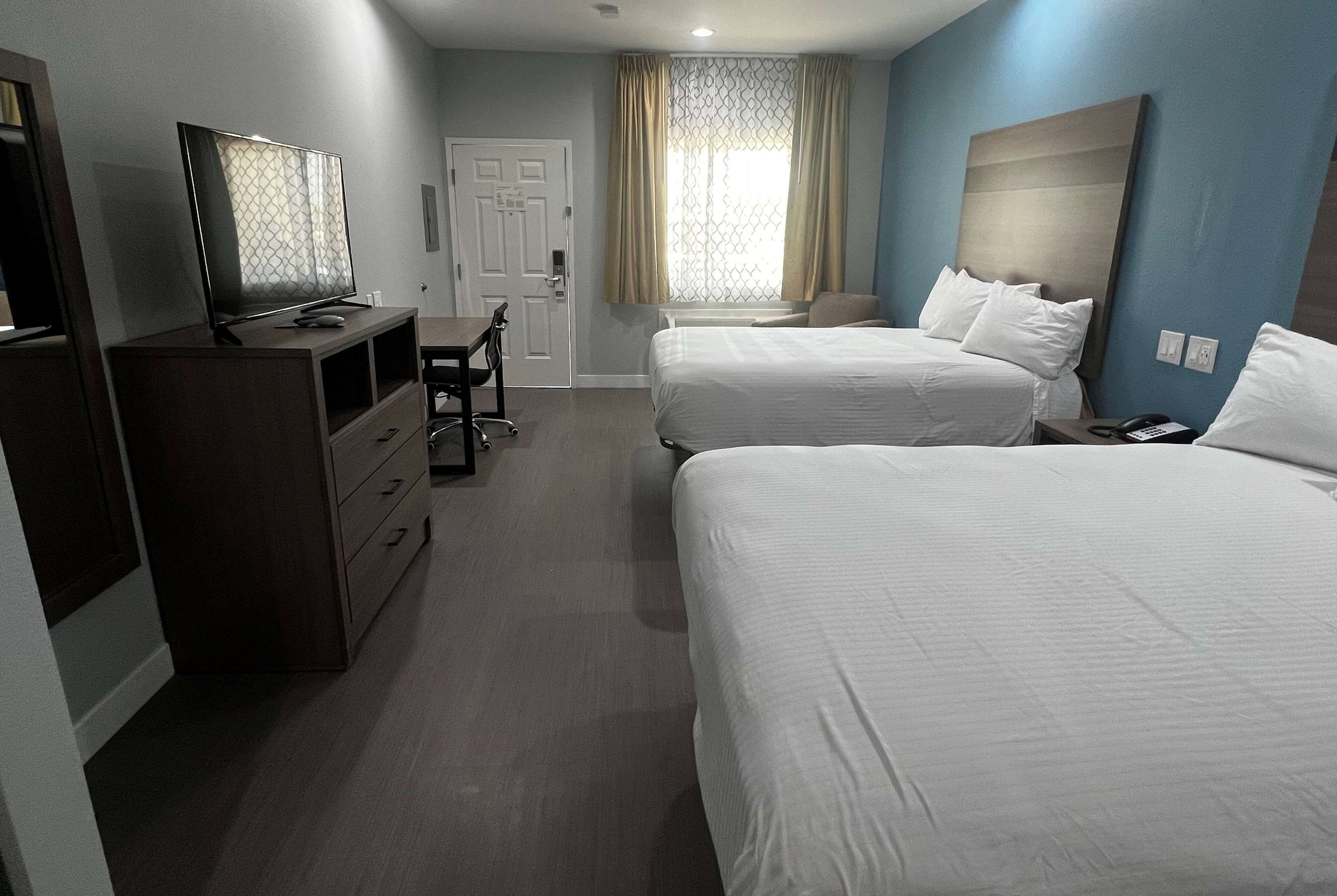 Ein Hotelzimmer mit zwei Betten, einem Fernseher, einem Schreibtisch und einem Sessel.