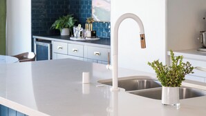 Eine moderne Küche mit weißer Arbeitsplatte, Spüle aus Edelstahl und Pendelleuchten.
