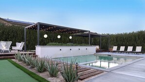 Ein moderner Poolbereich im Freien mit überdachter Lounge, Solaranlage und gepflegtem Rasen.