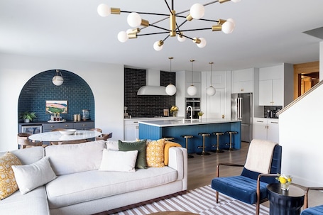 A modern kitchen with white cabinets, a blue island, and a black brick accent wall.