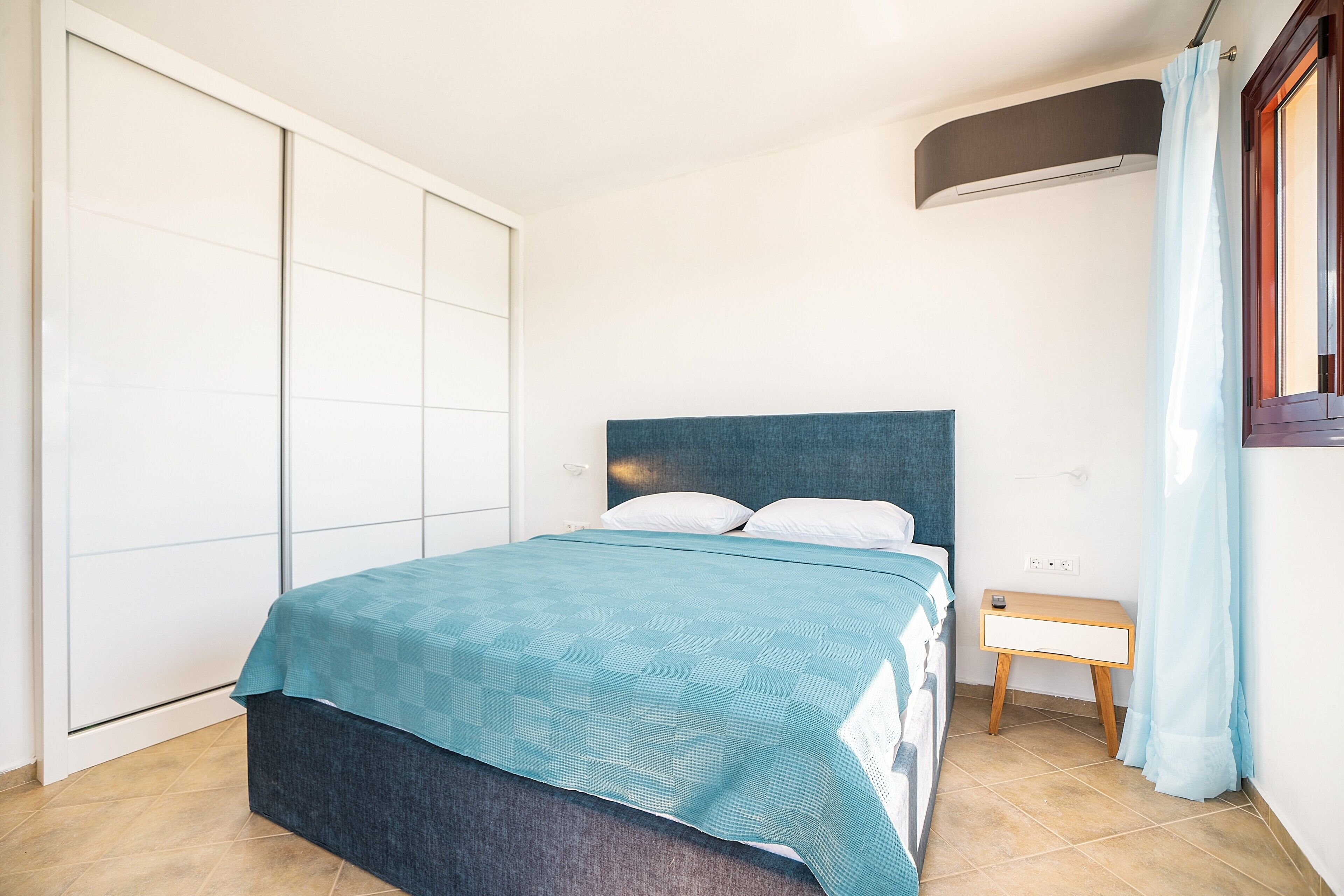 A bedroom with a bed, a bedside table, a wardrobe, and a window with curtains.