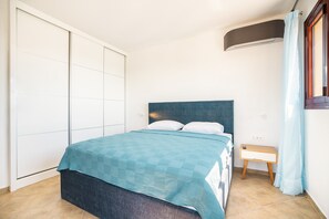 A bedroom with a bed, a bedside table, a wardrobe, and a window with curtains. - Country House ‘Sky Hills’ with Panoramic Sea Views, Wi-Fi, and Air Conditioning (Rhodes)