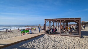 Una spiaggia con un molo di legno, persone che si rilassano e un cielo sereno.