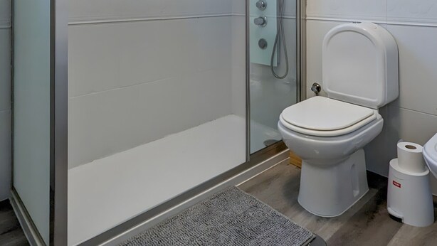 A modern bathroom with a glass-enclosed shower, a toilet, and a small rug on the floor. - Apartment 'Costa Nova Ocean View' with Sea View, Wi-Fi and Air Conditioning (Gafanha da Encarnação)