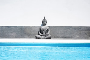 A statue of a seated figure by a pool.