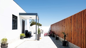 A modern outdoor patio with a white building, a wooden fence, and potted plants. - Holiday Home 'La Posada' with Pool, Garden, Terrace & Wi-Fi (Conil de la Frontera)