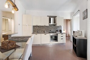 Une cuisine moderne avec des armoires blanches, un pare-feu en pierre, une hotte de cuisinière en acier inoxydable et un four encastré.