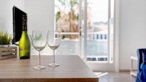 A wooden table with a wine bottle and two glasses, a potted plant, and a view of a balcony with palm trees. - Vacation Home 'Bonito Apartamento Cristian Playa' with Balcony & Wi-Fi (Arona)