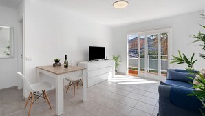 A modern living room with a TV, white furniture, a balcony with a city view, and a plant. - Vacation Home 'Bonito Apartamento Cristian Playa' with Balcony & Wi-Fi (Arona)