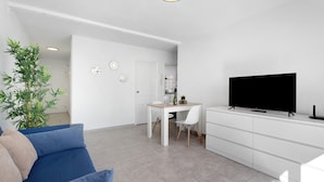 A modern living room with a sofa, a dining table with chairs, a TV, and a plant. - Vacation Home 'Bonito Apartamento Cristian Playa' with Balcony & Wi-Fi (Arona)