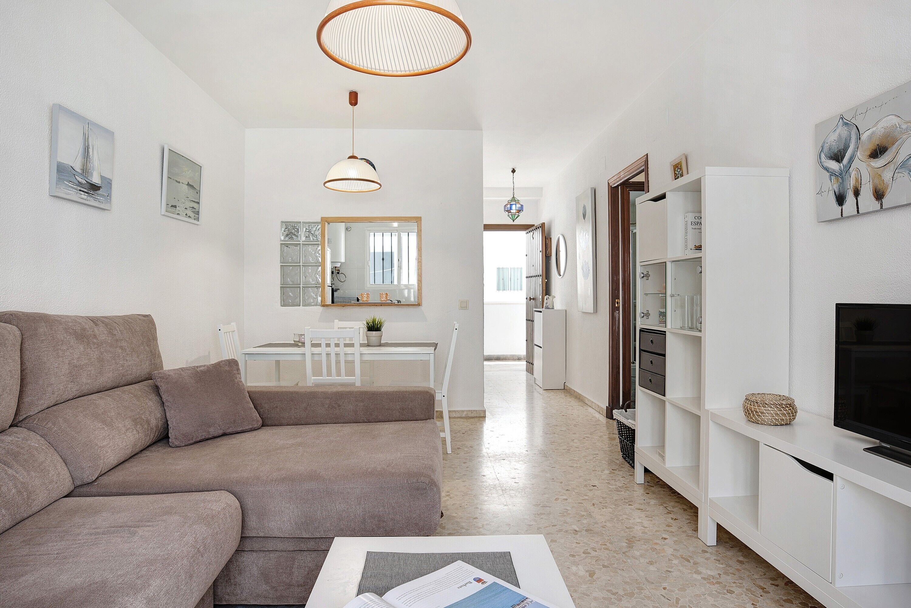 Una sala de estar moderna con un sofá, una zona de comedor y un televisor sobre un mueble blanco.
