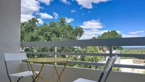 Ein Balkon mit weißer Brüstung, einem kleinen runden Tisch und zwei weißen Stühlen.
