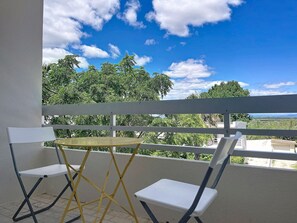 Un balcon avec une balustrade blanche, une petite table ronde et deux chaises blanches.