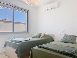 A room with two beds, a window, an air conditioning unit, and a radiator.