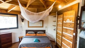 Un dormitorio con cama, techo de madera, mosquitera colgante, mesita de noche, cómoda y armario de madera.