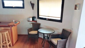 Una cocina compacta con barra, dos sillas de mimbre, una mesita redonda y un taburete de madera.
