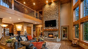 A spacious living room with a fireplace, leather sofa, and a large TV mounted on a stone wall.