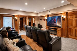 A home theater with leather recliners, a large flat-screen TV, and wooden paneling.