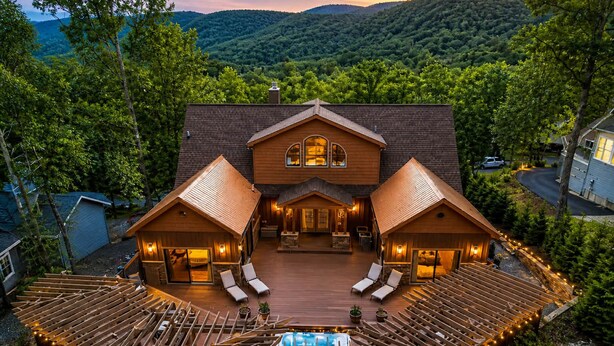A large wooden house with a pool, surrounded by a deck with lounge chairs.